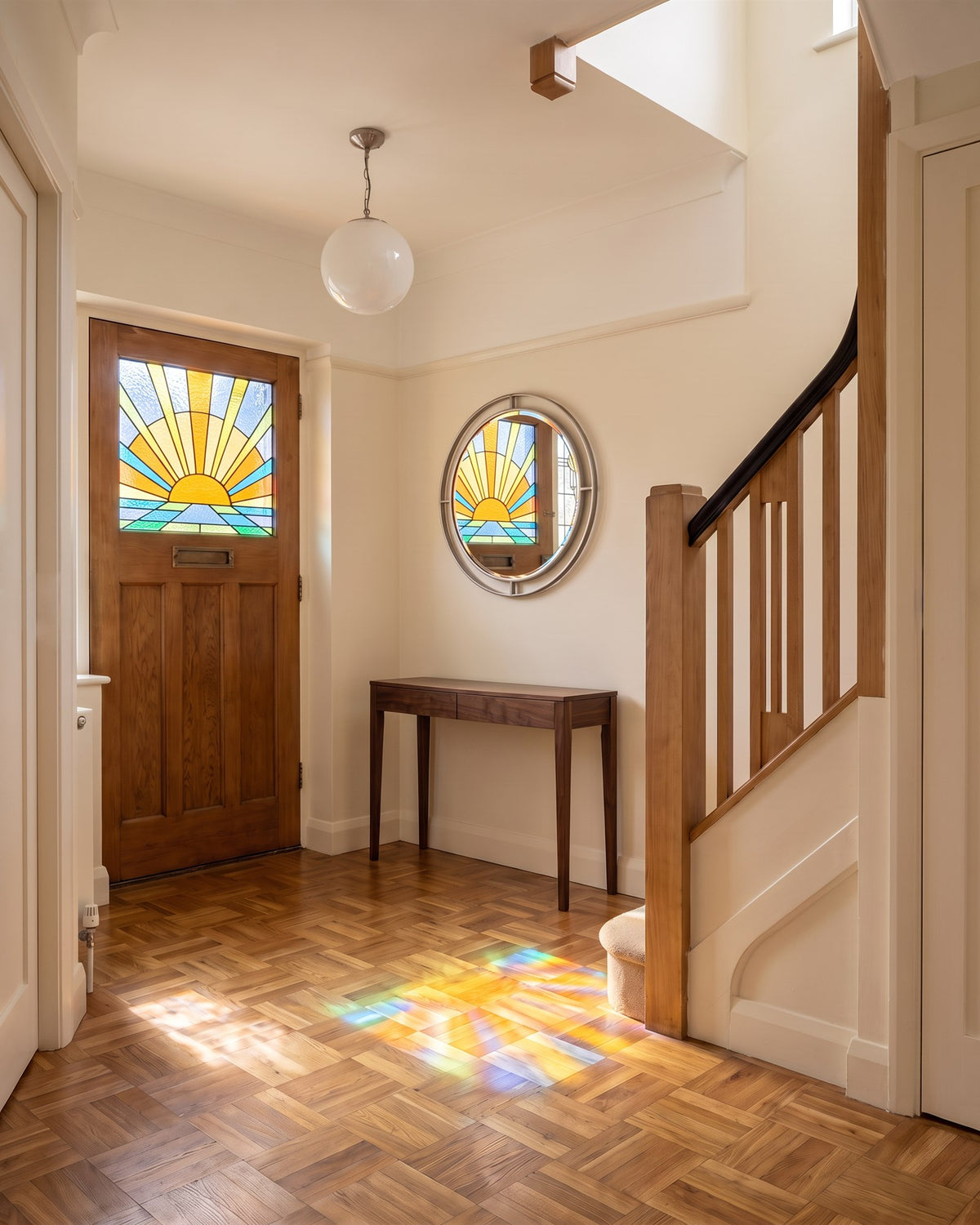 1930s entrance hall with basket-weave parquet, an oak front door with a stained glass sunrise and coloured light falling on the floor