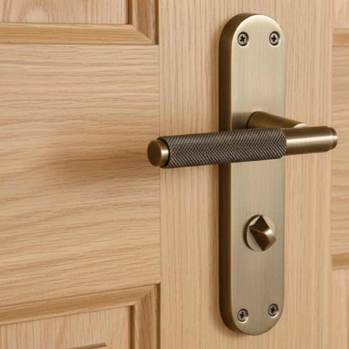 Antique brass knurled lever and privacy turn on a rounded backplate, fitted to a light oak panelled door