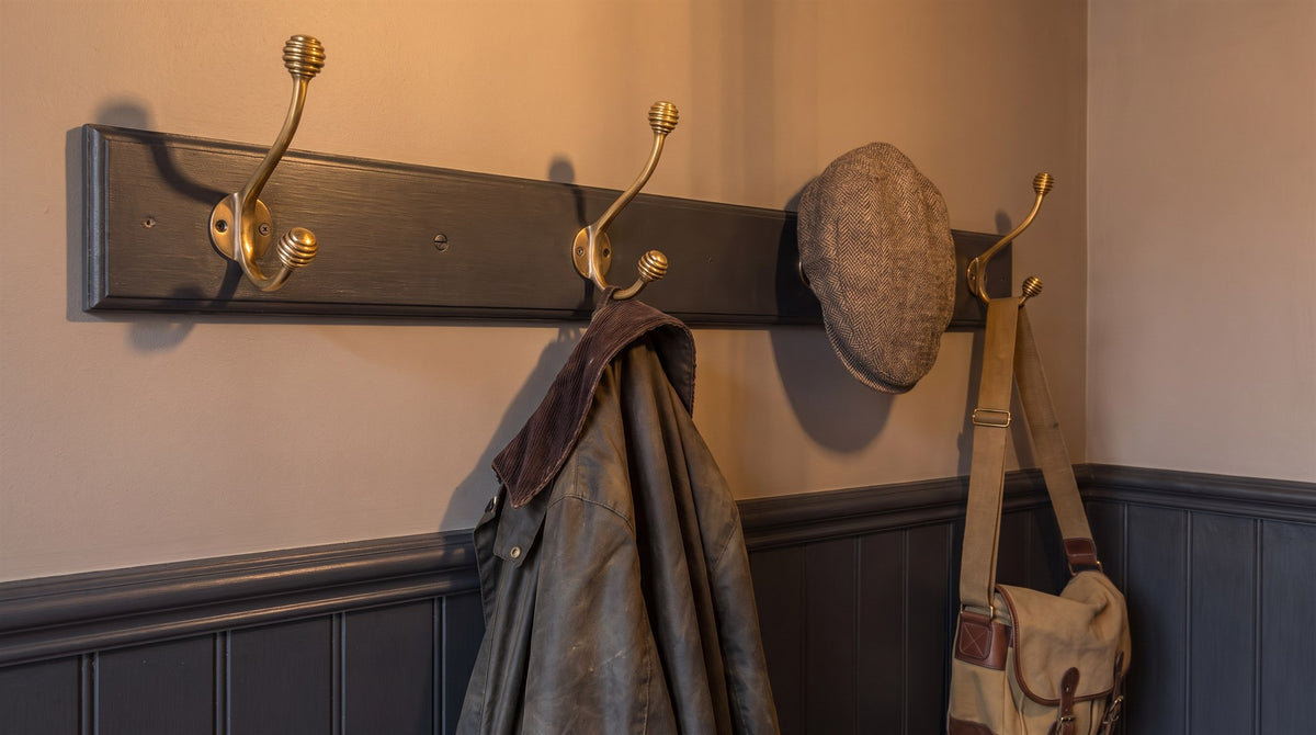 Row of aged brass beehive hat and coat hooks with coats hanging, above off-black tongue-and-groove panelling in a Victorian hall