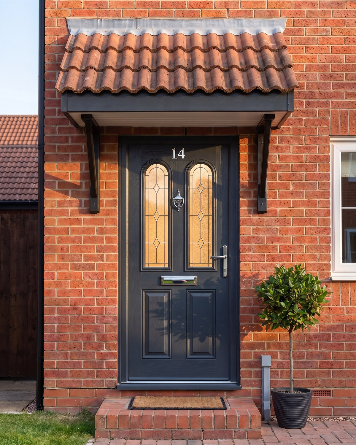 Anthracite composite front door under a tiled canopy in warm evening light, chrome knocker, letter plate and lever glowing against the grey