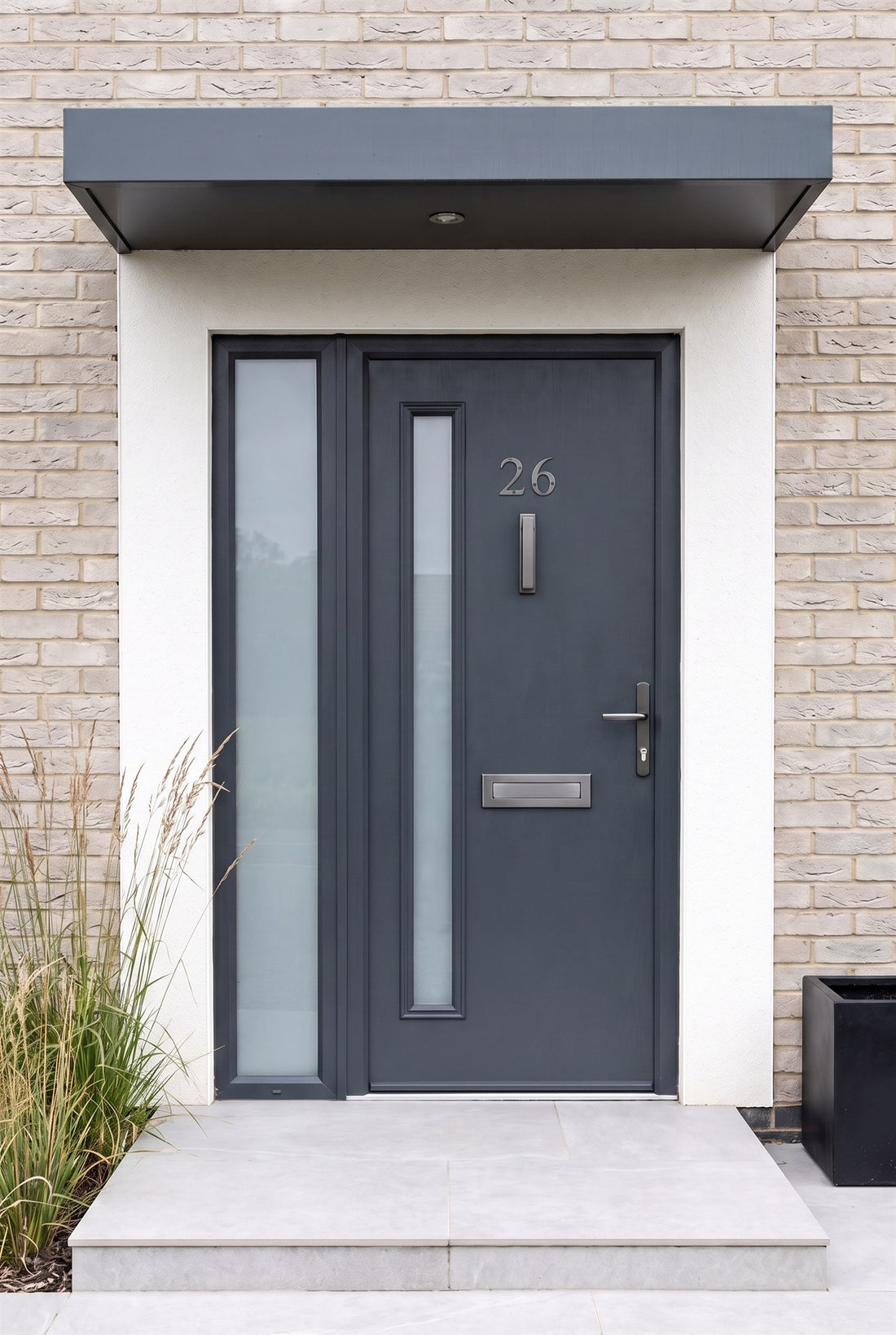 Anthracite grey composite front door with a frosted glass strip and side light under a flat canopy, fitted with graphite numbers 26, a bar knocker, shield letter plate and Windsor lever handle