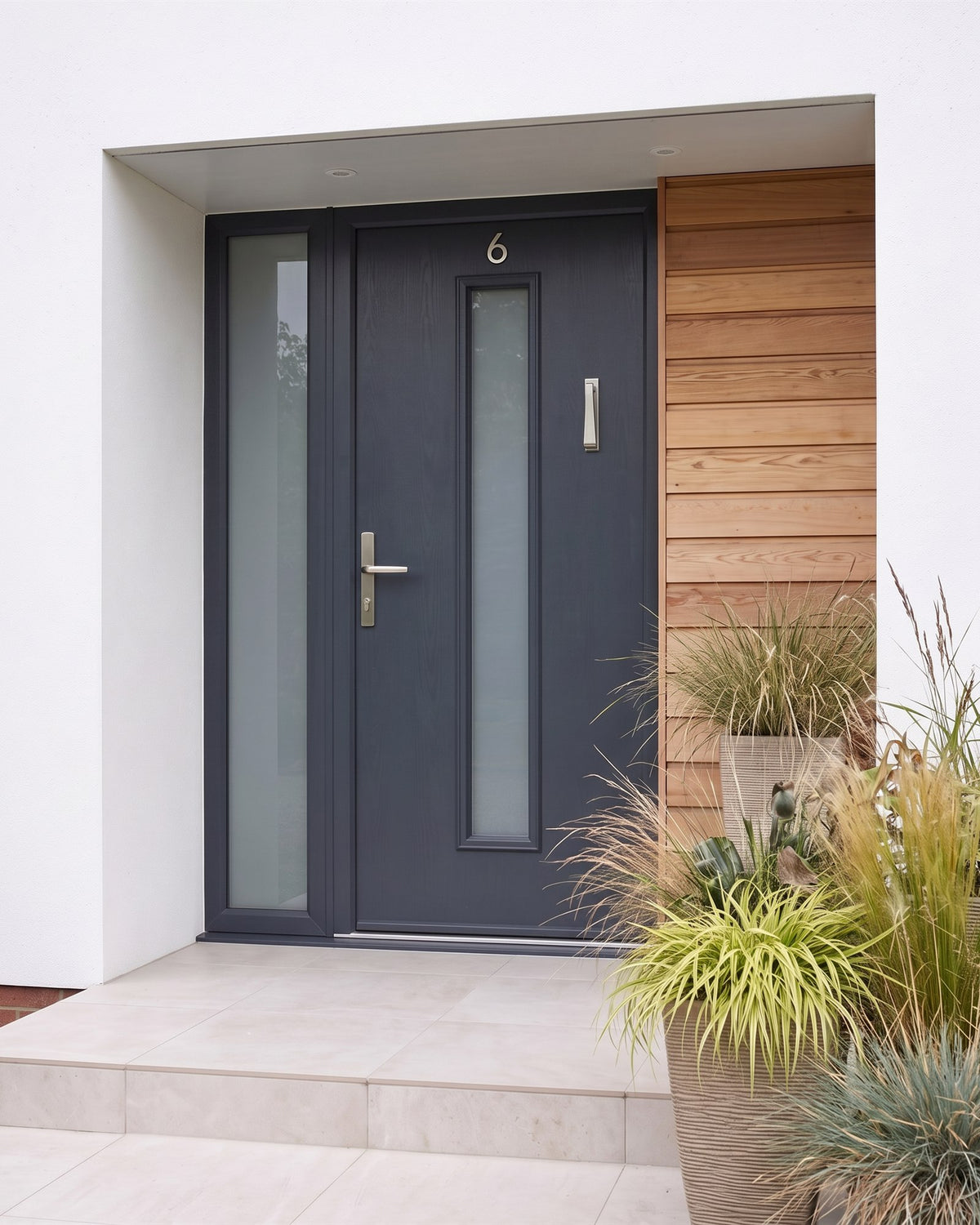 Anthracite composite front door with a glazed sidelight in a white render and larch facade, fitted with a satin nickel Bauhaus multipoint handle, a slim knocker beside the glazed strip and number 6