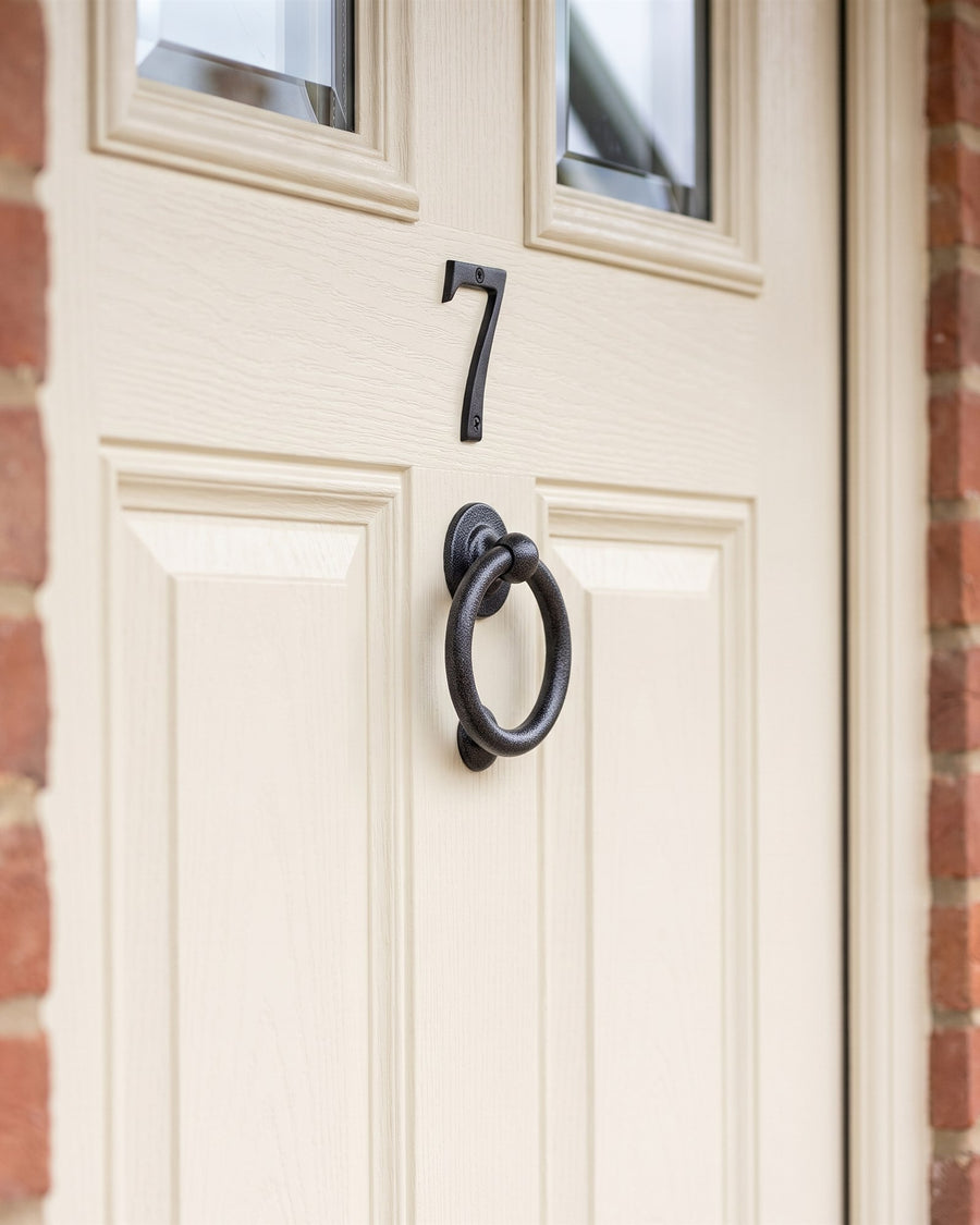 Antique black house number 7 above an antique black ring knocker on a cream composite front door