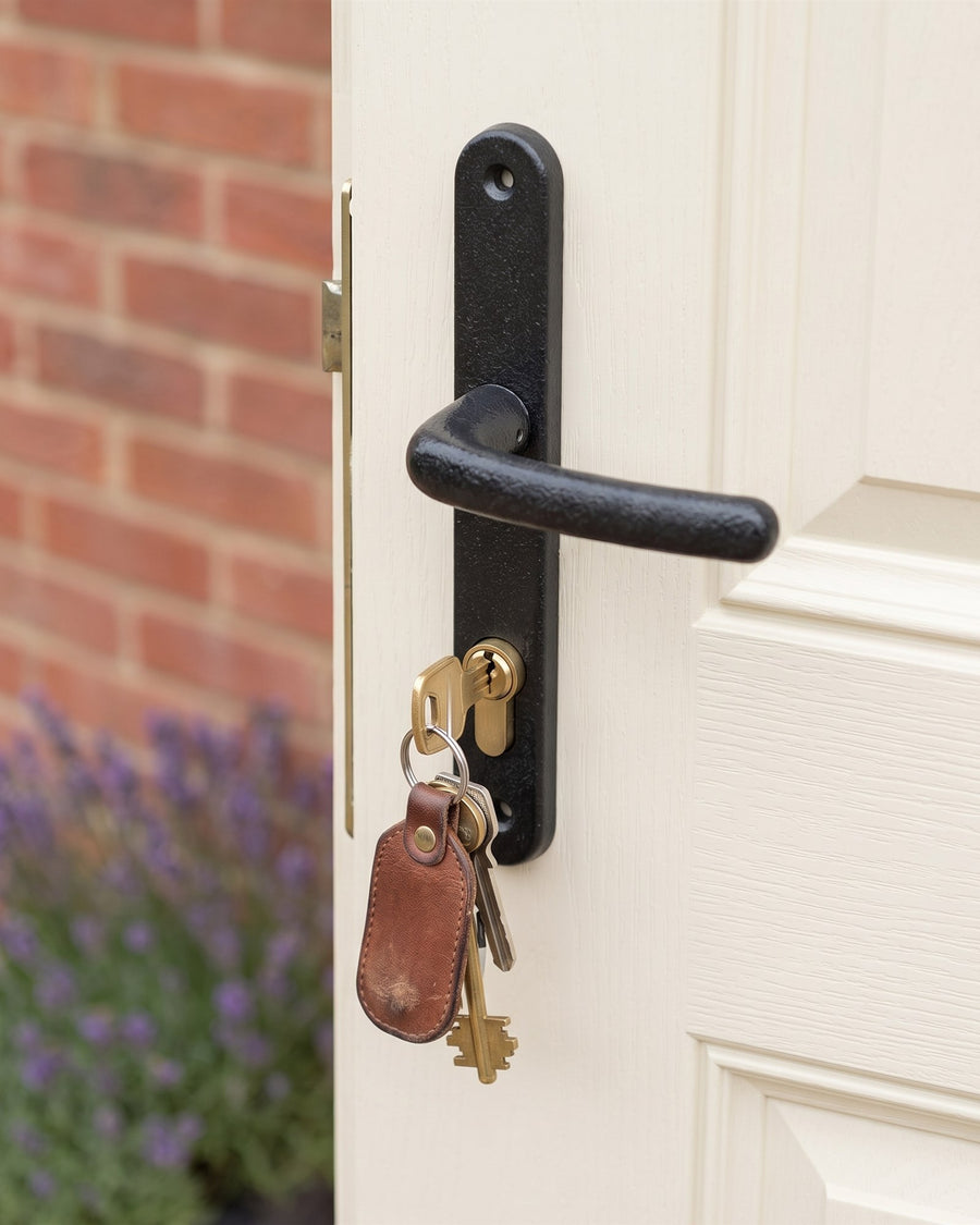 Keys on a leather fob in the brass euro cylinder below an antique black uPVC lever handle on a cream door