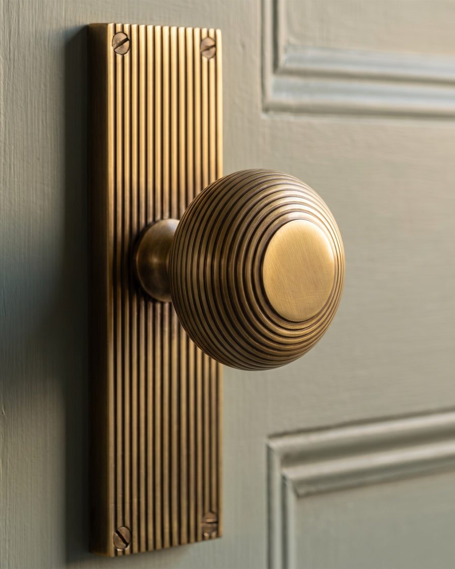 Close-up of an antique brass beehive door knob on a reeded backplate, low light picking out each ring