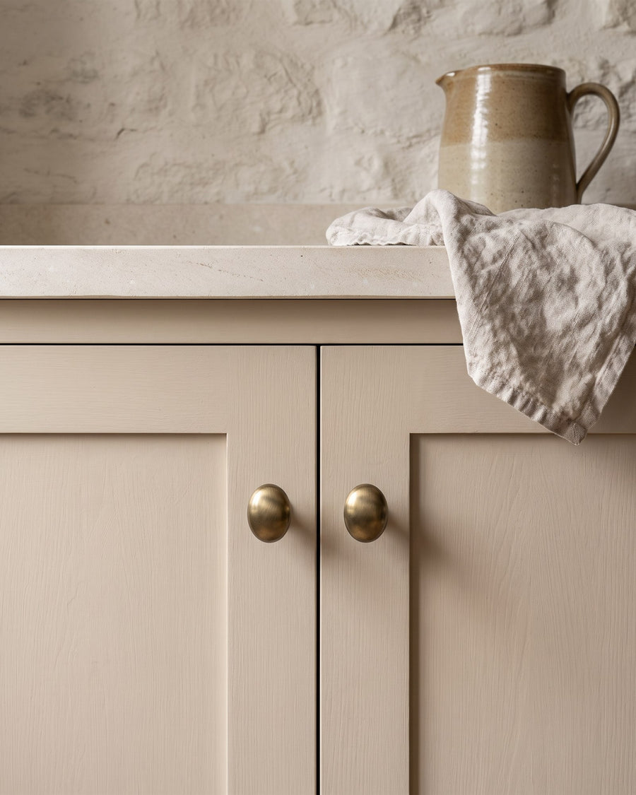 Antique brass bun knobs on a mushroom painted shaker cupboard under a limestone top