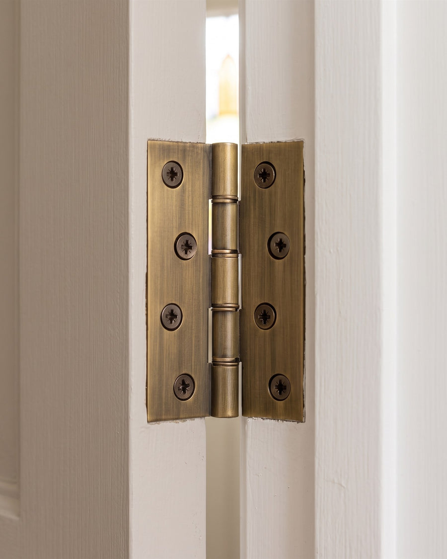 Antique brass butt hinge joining a greige panelled door to its frame
