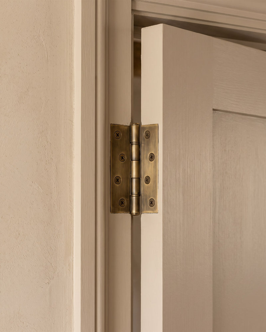 Antique brass butt hinge on a mushroom-painted door against a limewashed wall