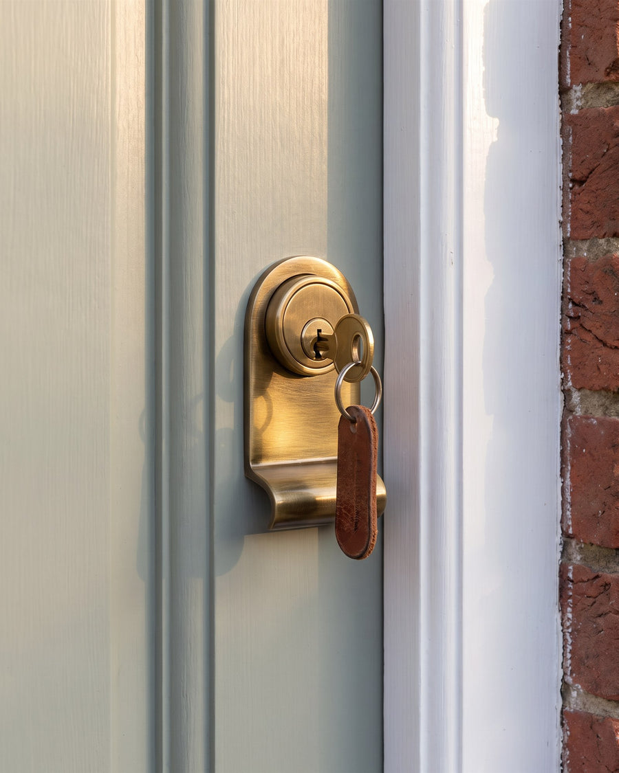 Antique brass cylinder pull around a round brass rim cylinder with a key and leather tag, on a grey-green cottage door