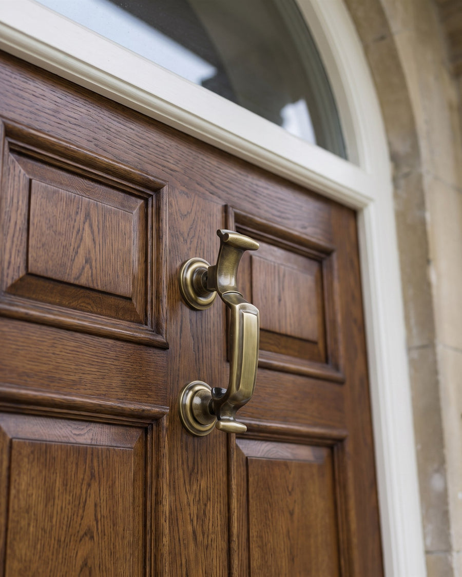 Antique brass doctor knocker on a raised and fielded panel of a stained oak front door below a fanlight