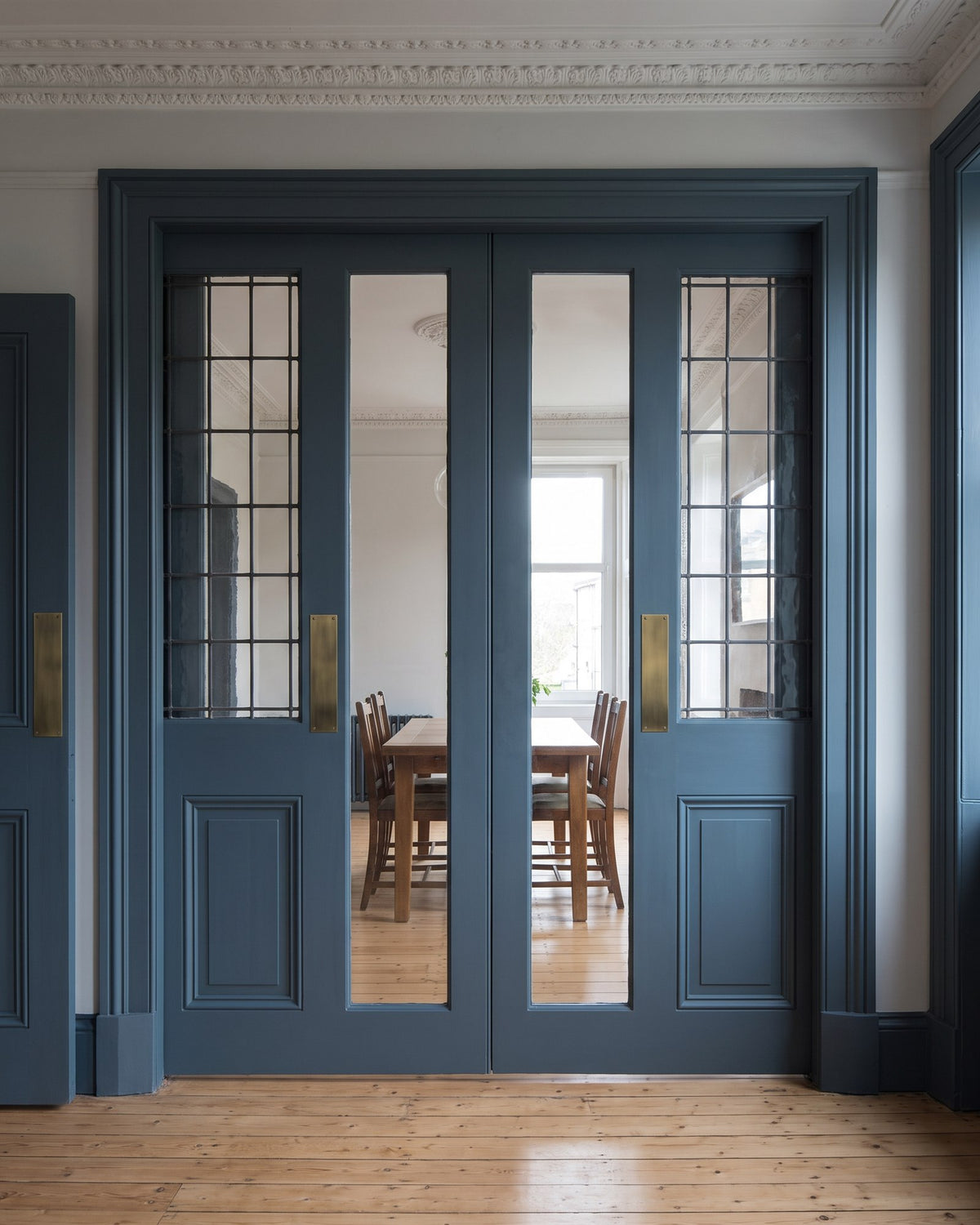 Blue-grey glazed double doors between a tenement front room and dining room, with antique brass finger plates and no handles