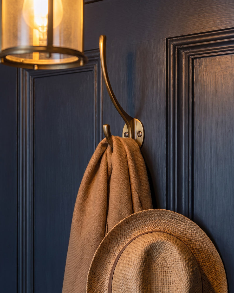 Antique brass hat and coat hook holding a camel scarf and straw hat on a dark panelled door