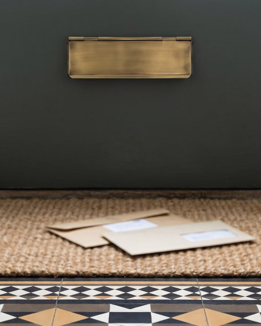 Antique brass interior flap hanging over the letter opening on the inside of a green front door above an encaustic tiled hall floor