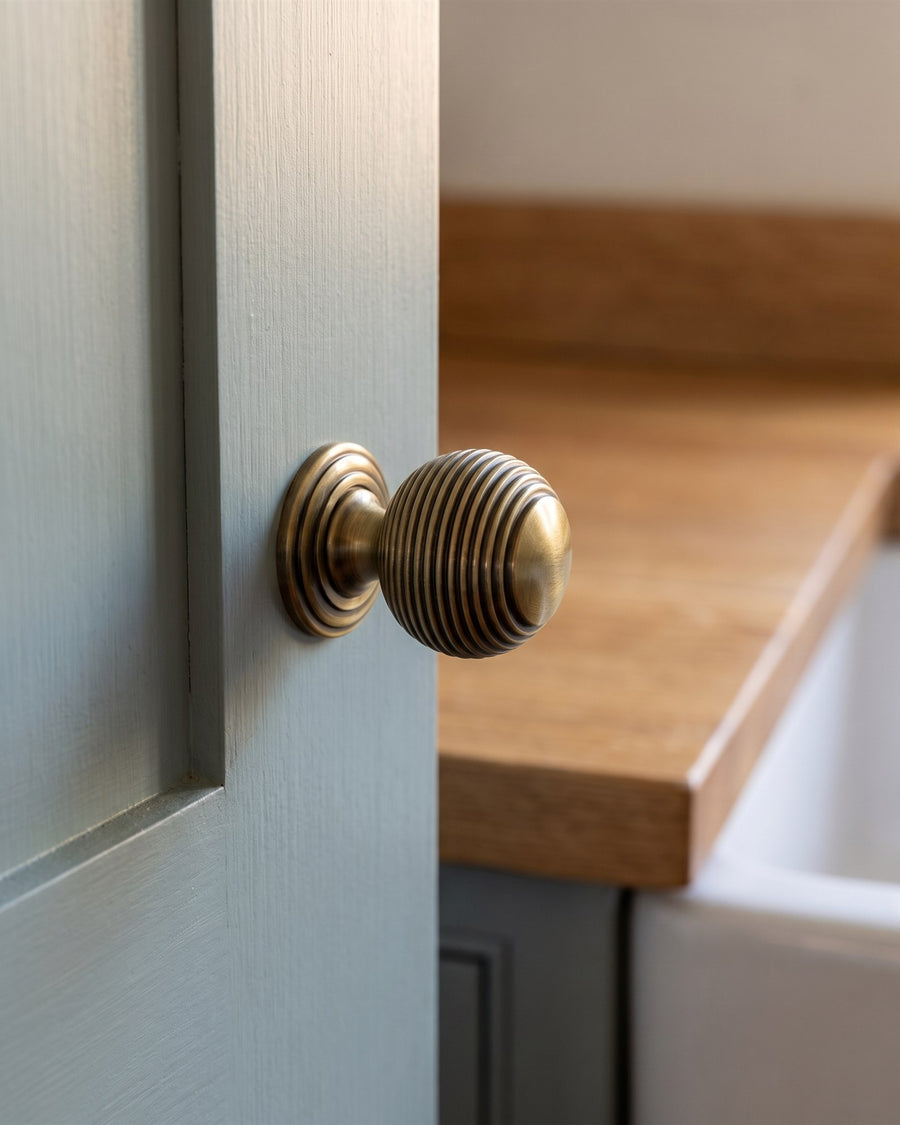 Close-up of an antique brass reeded ball cupboard knob on a painted kitchen cabinet door