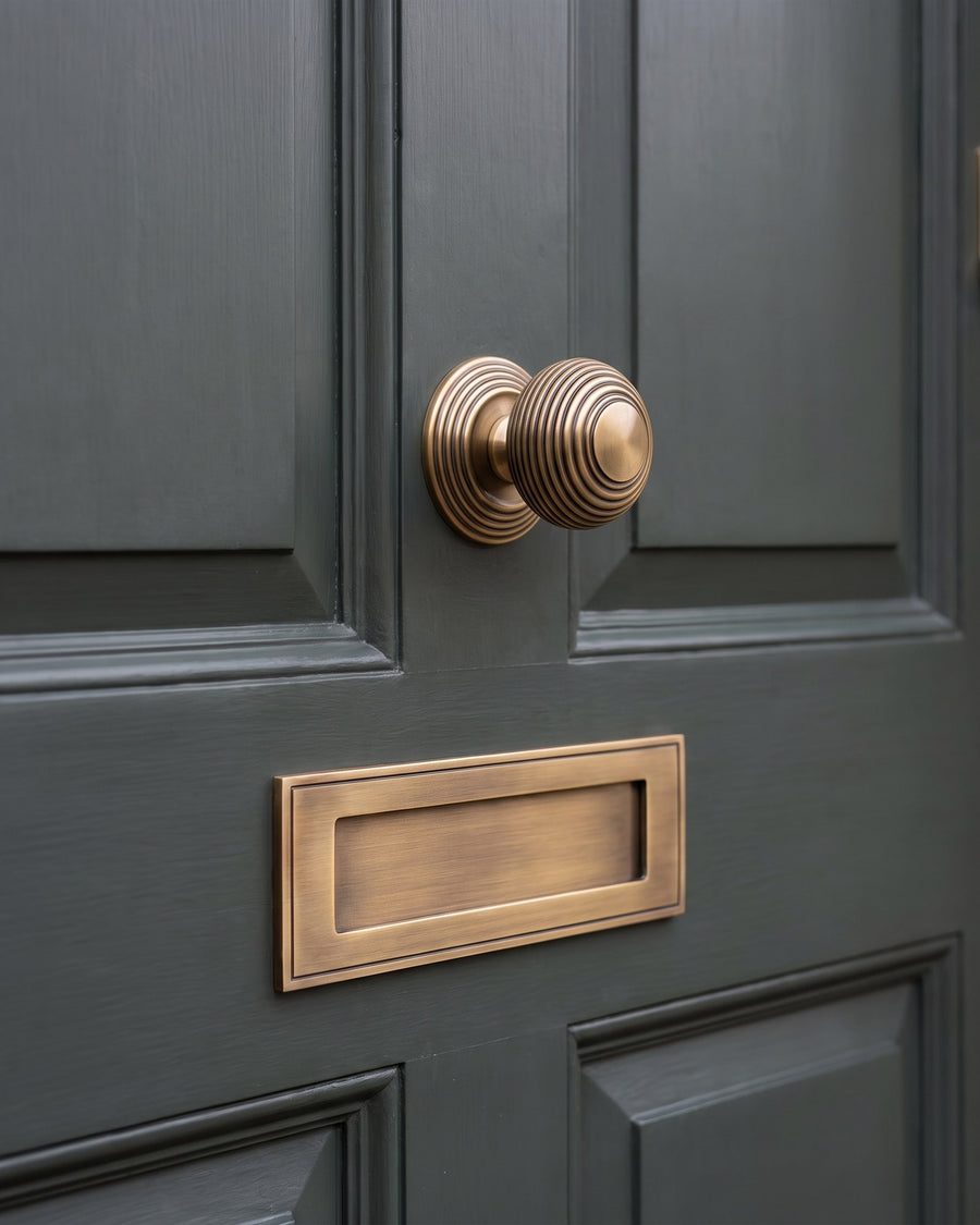 Antique brass reeded beehive centre knob above a plain antique brass letter plate on a smoky green panelled door
