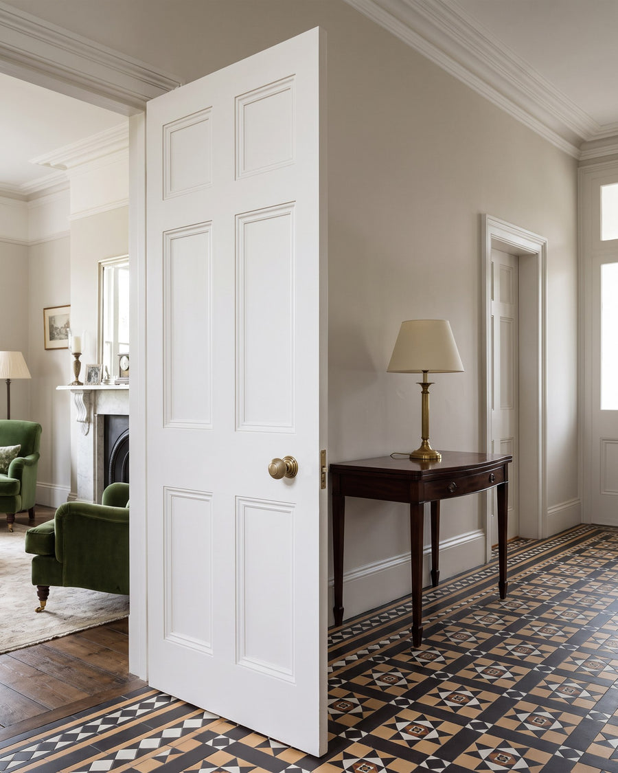 Antique brass reeded mortice knob on a white six-panel door in a Victorian hall with an encaustic tiled floor, opening onto a drawing room