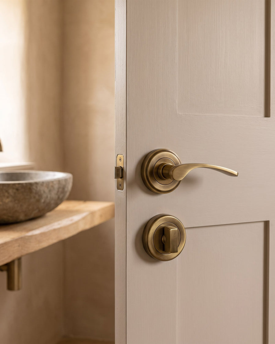 Antique brass Sophia lever and turn and release on a mushroom-painted bathroom door, stone basin on an oak plank beyond