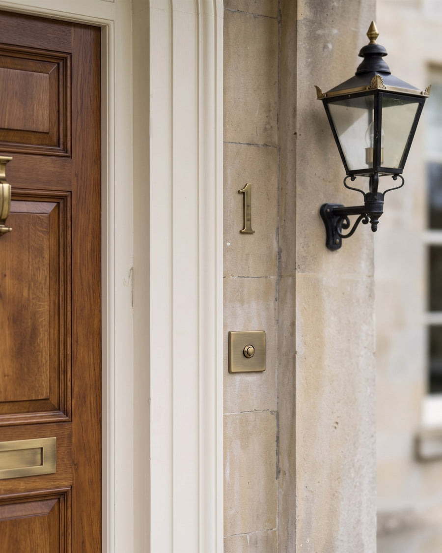 Square antique brass bell push and house number 1 on a pale stone door surround beside a black and brass carriage lantern