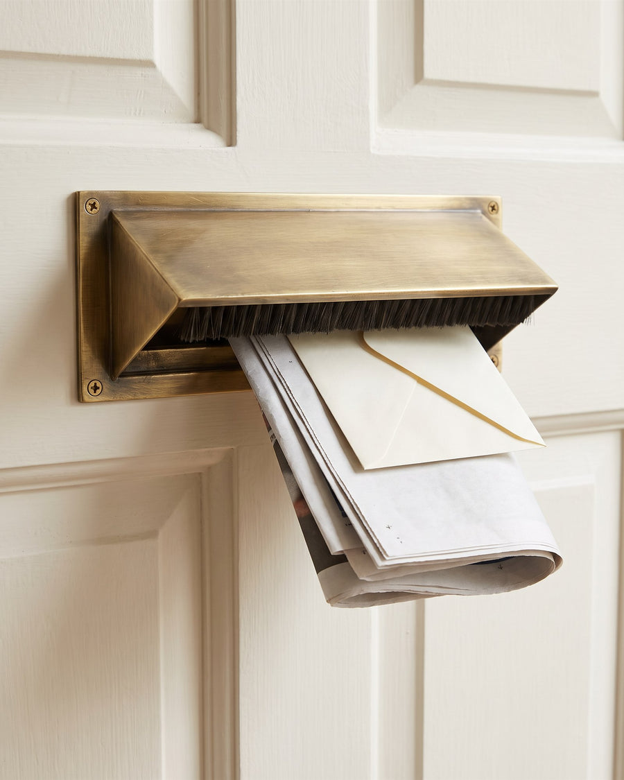 Antique brass letter tidy with a brush draught excluder on the inside of a door, a newspaper and envelope dropping out of its open base