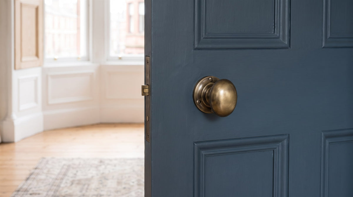 Antique brass Victoria mortice knob and covered escutcheon on a tall blue-grey panelled tenement door