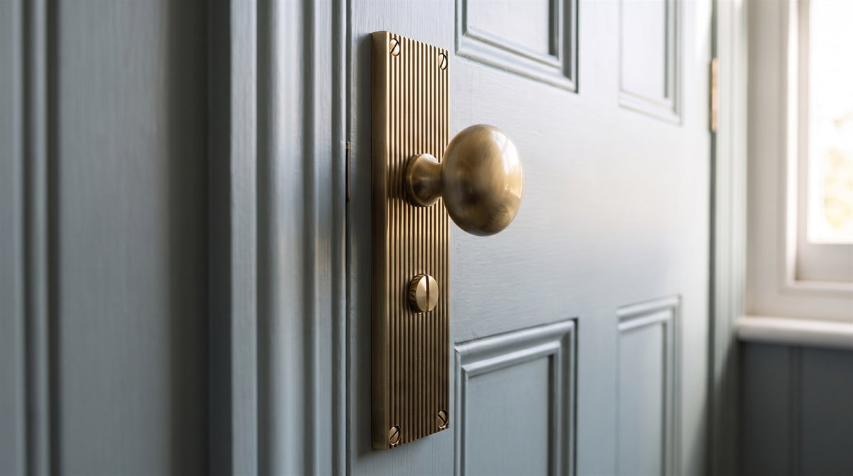 Antique brass round knob on a finely reeded bathroom backplate with a thumbturn below, on a grey-blue painted panelled door