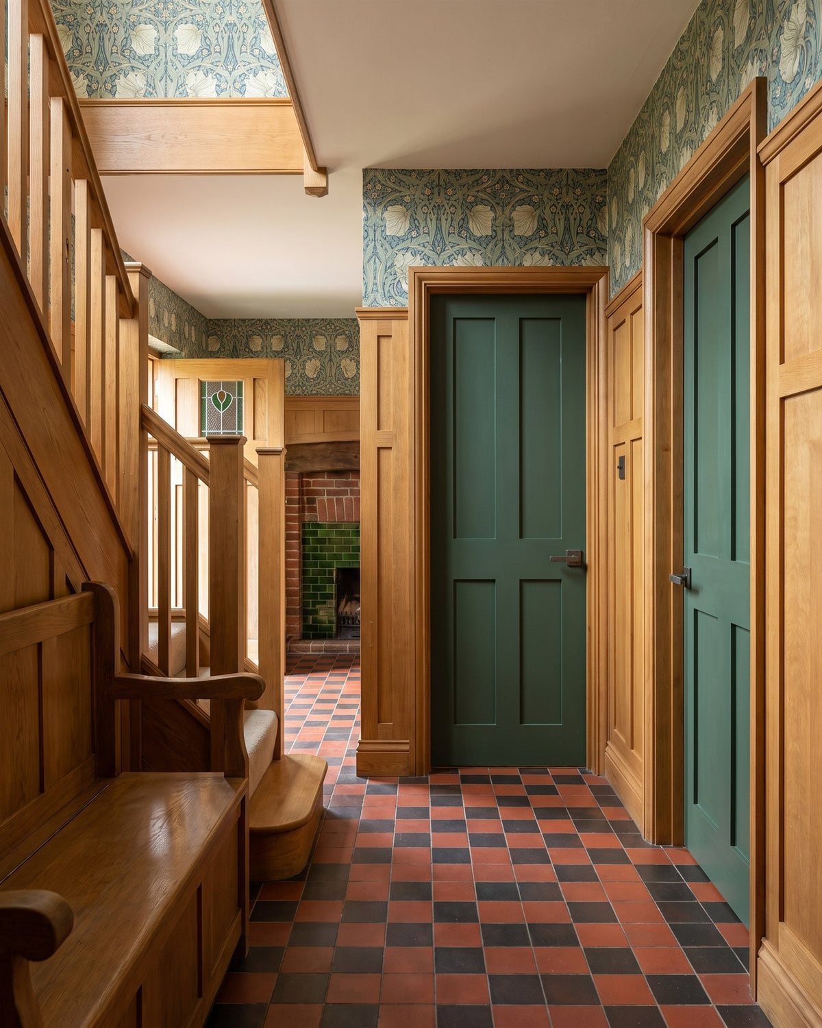 Arts and Crafts hall with oak panelling, William Morris wallpaper, a red and black quarry-tiled floor, an oak settle and deep green doors with pewter levers