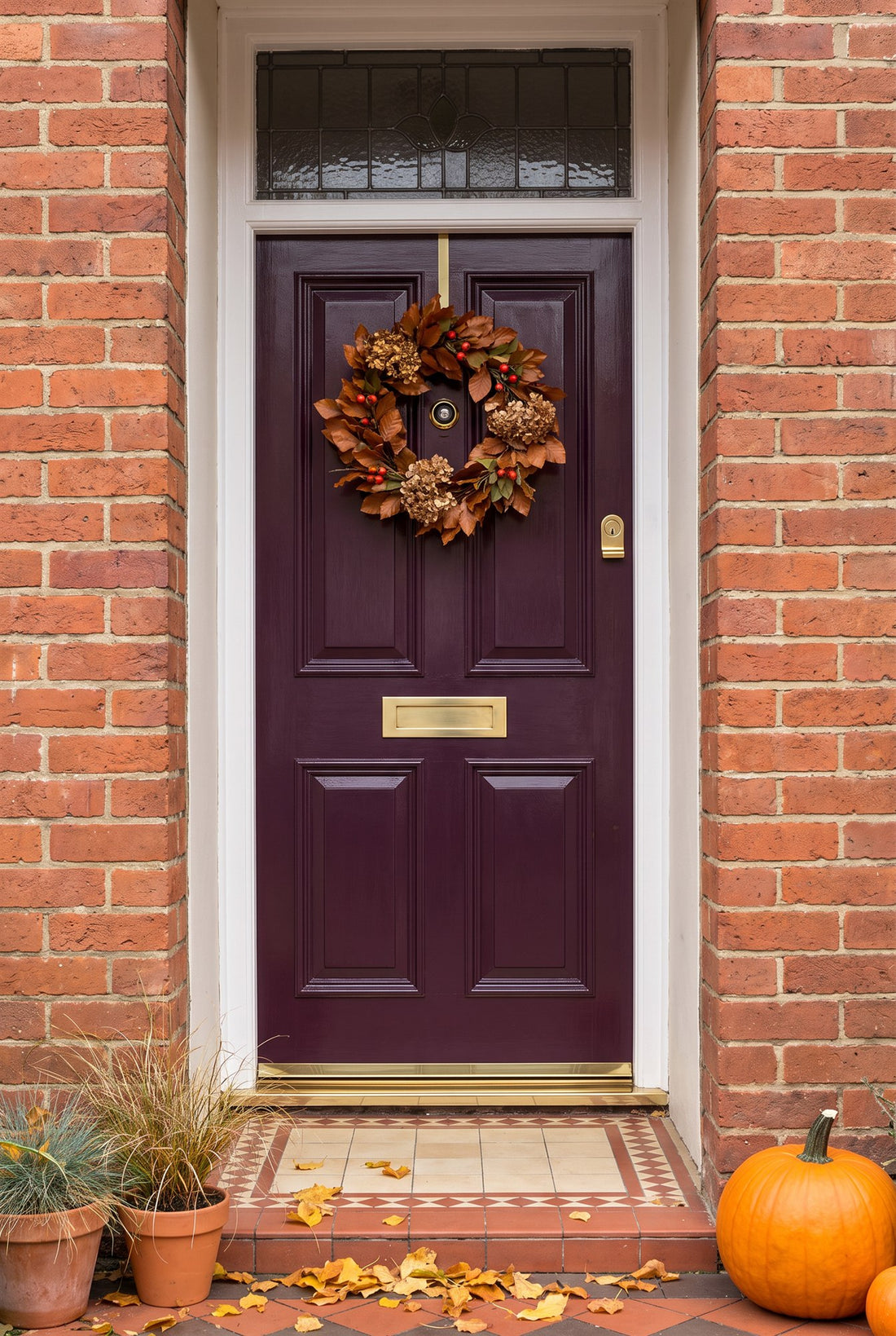 Aubergine Edwardian front door under a leaded fanlight with an autumn wreath, fitted with a polished brass viewer, letter plate and cylinder pull, a gold rain deflector and a polished brass threshold strip on the tiled step