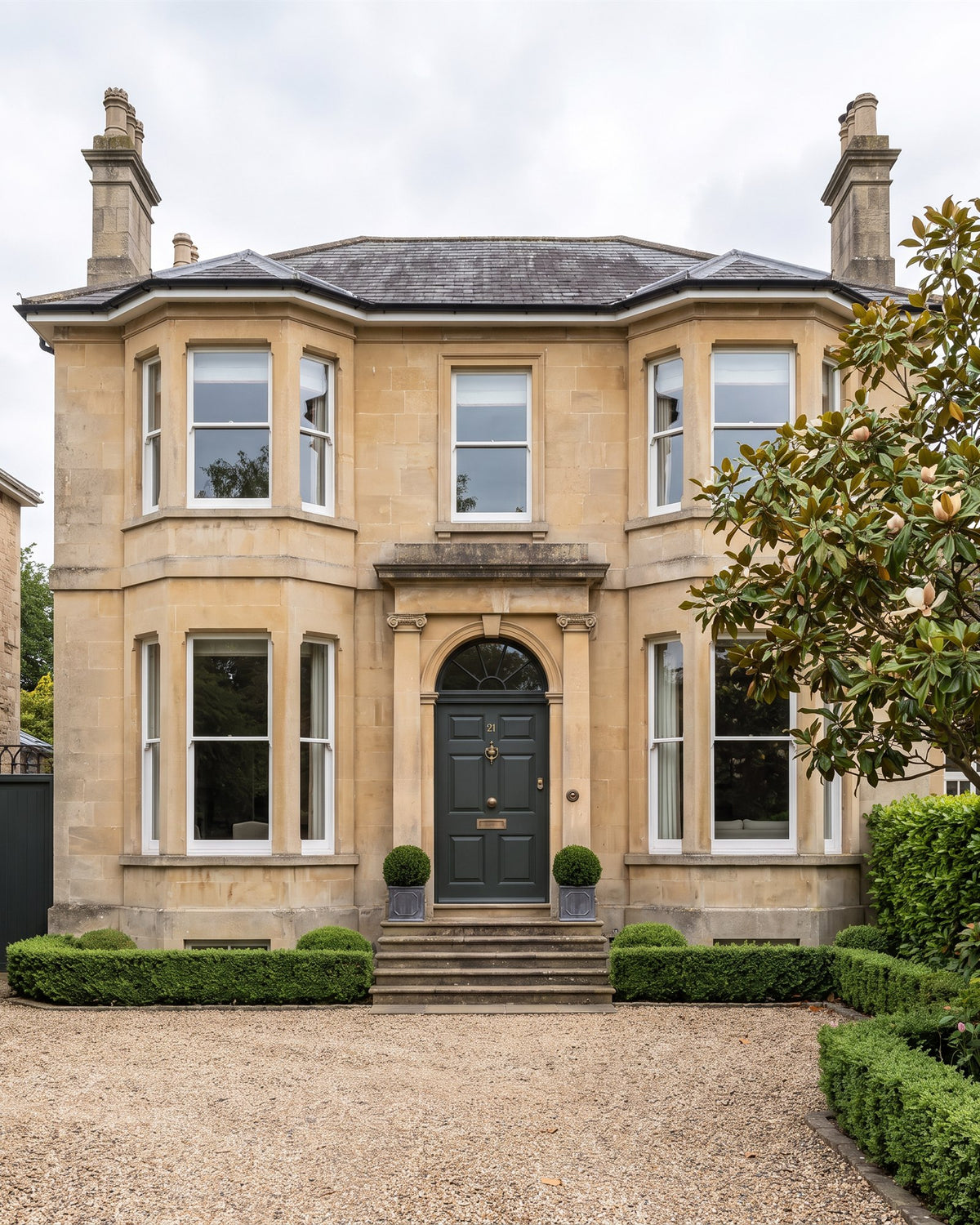 Detached Victorian villa in honey Bath stone with canted bays, a pilastered doorcase and fanlight over a smoky green door, stone steps, box balls and a gravel forecourt