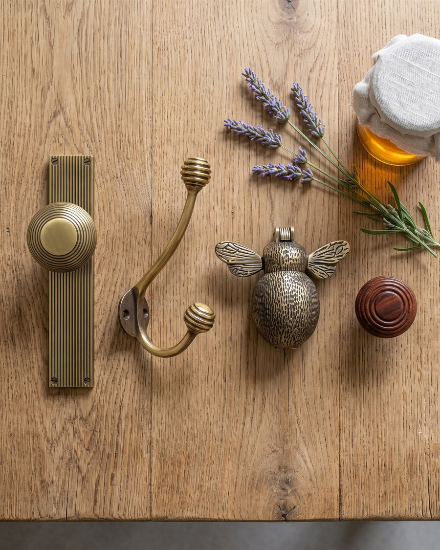 Beehive knob on reeded plate, beehive coat hook, bumble bee knocker and rosewood beehive cabinet knob laid out on a scrubbed oak table with lavender and honey