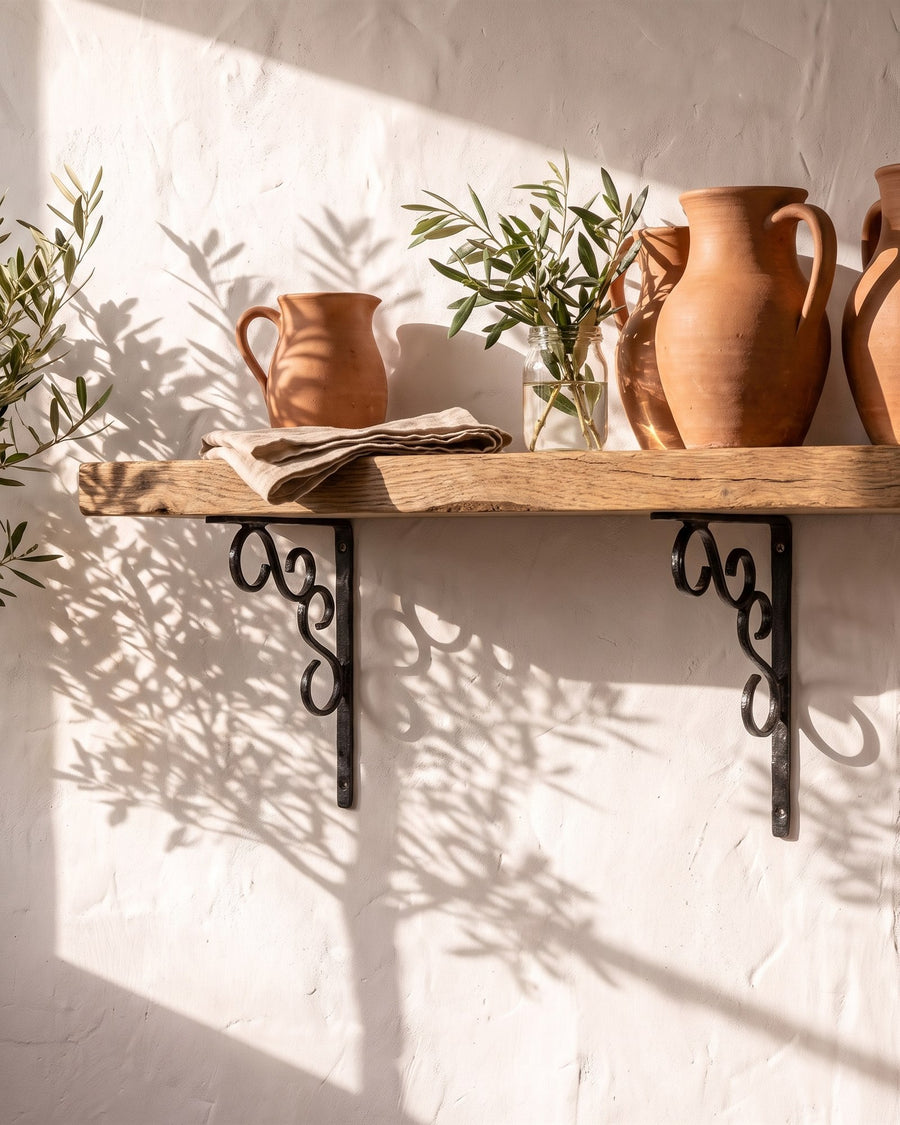 Black antique iron ornate shelf brackets holding an oak shelf of terracotta jugs on a limewashed wall