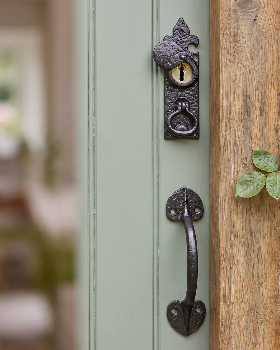 Black iron rim cylinder pull with a swinging key cover above a heart-ended black iron pull handle on a green boarded door