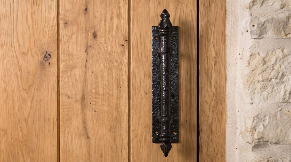 Black antique iron pull handle with spear finials fixed upright beside the opening edge of a honey oak plank door
