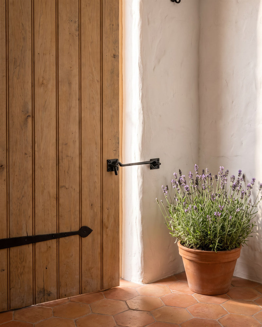 Black iron rustic cabin hook holding an oak plank door open against a limewashed wall