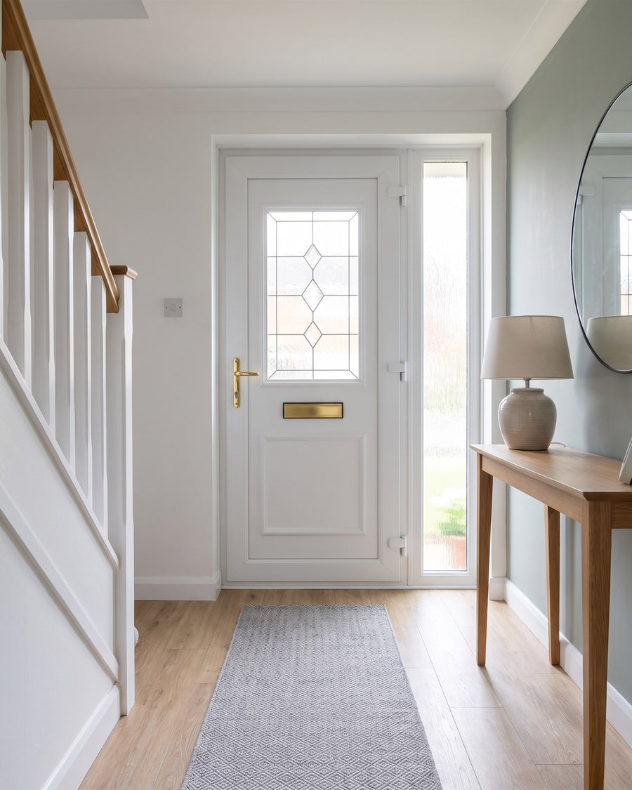 Bright hallway with oak-effect flooring, a white staircase and a sage feature wall, looking at the inside of the white uPVC front door
