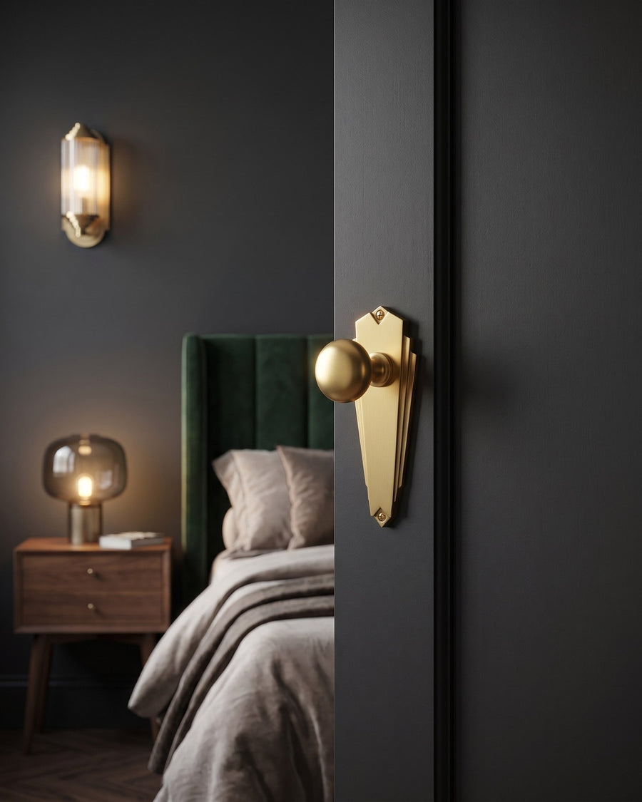 Broadway satin brass knob on a charcoal bedroom door, green velvet headboard and smoked glass lamp beyond