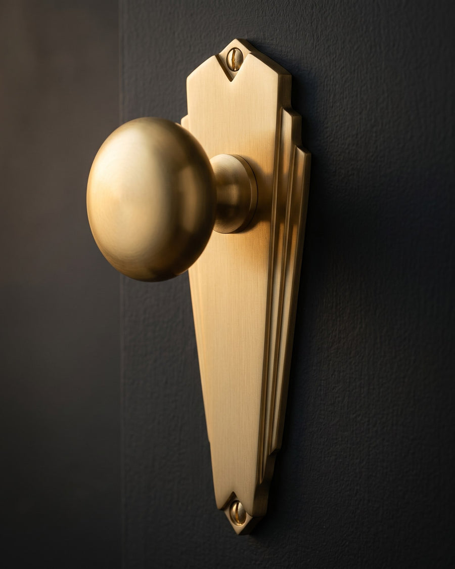 Close-up of the satin brass Broadway knob on its tapering tiered backplate against near-black paint