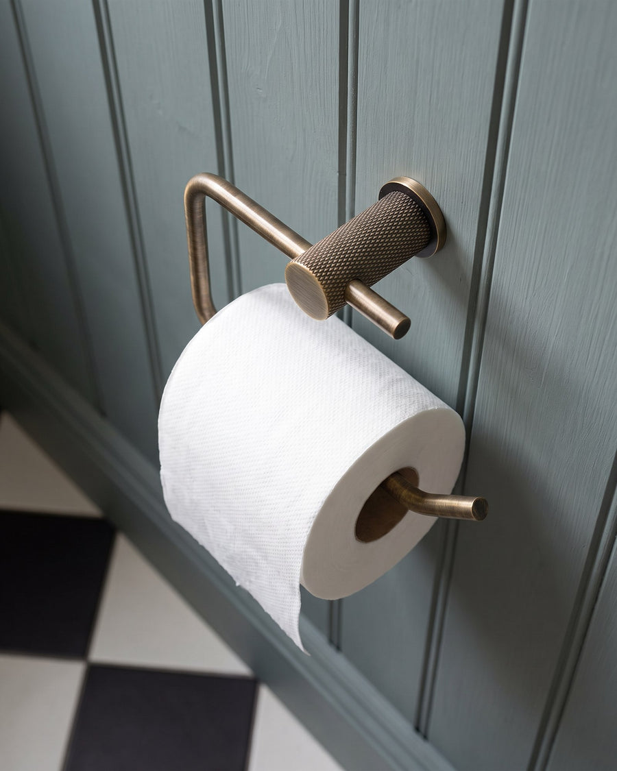 Knurled antique brass Brunel toilet roll holder on grey-blue panelling above a black and white tiled floor