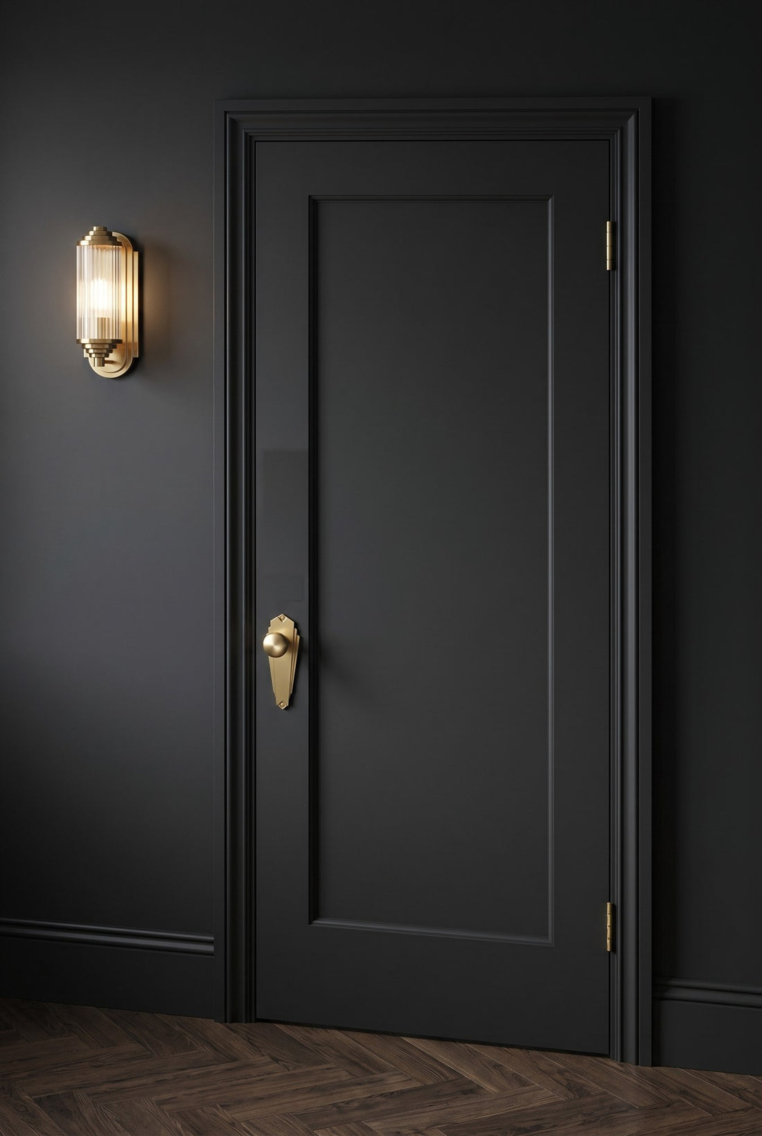 Charcoal single-panel door with a satin brass Broadway knob on plate and satin brass hinges beside a ribbed-glass Art Deco wall light