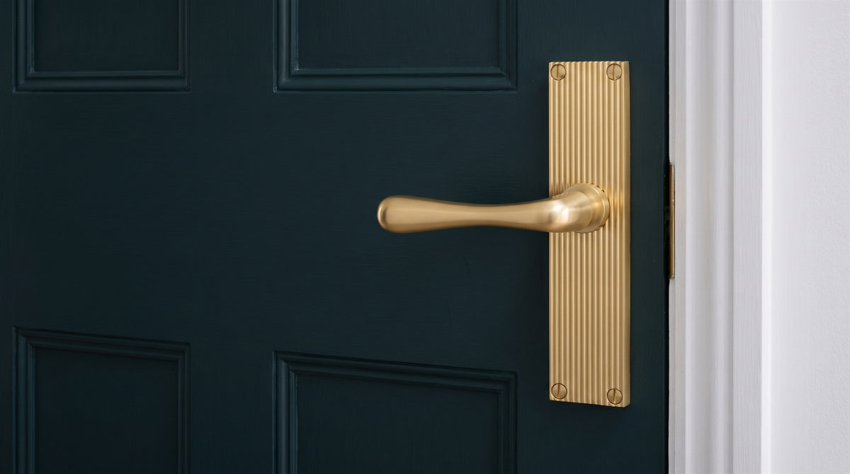 Satin brass reeded lever handle on a tall narrow reeded backplate on a deep inky green panelled door