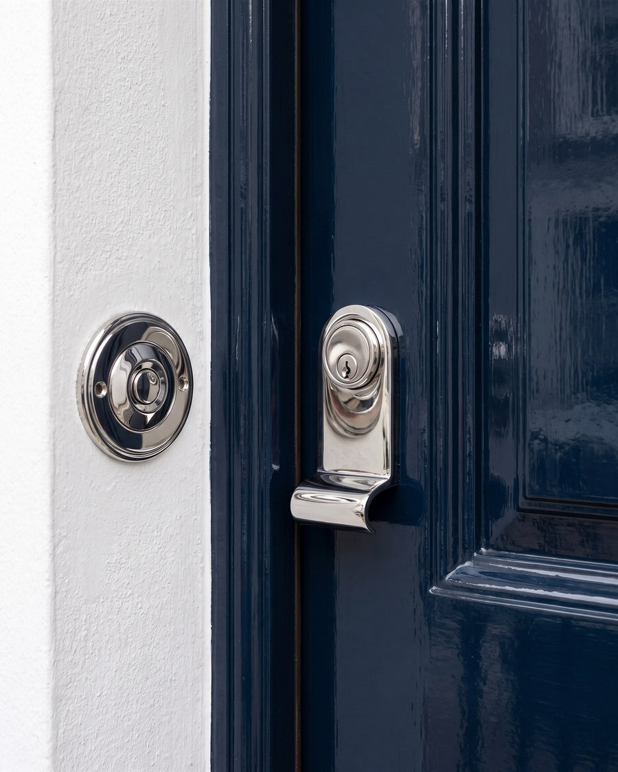 Polished chrome circular bell push on white stucco beside a chrome cylinder pull on a navy door