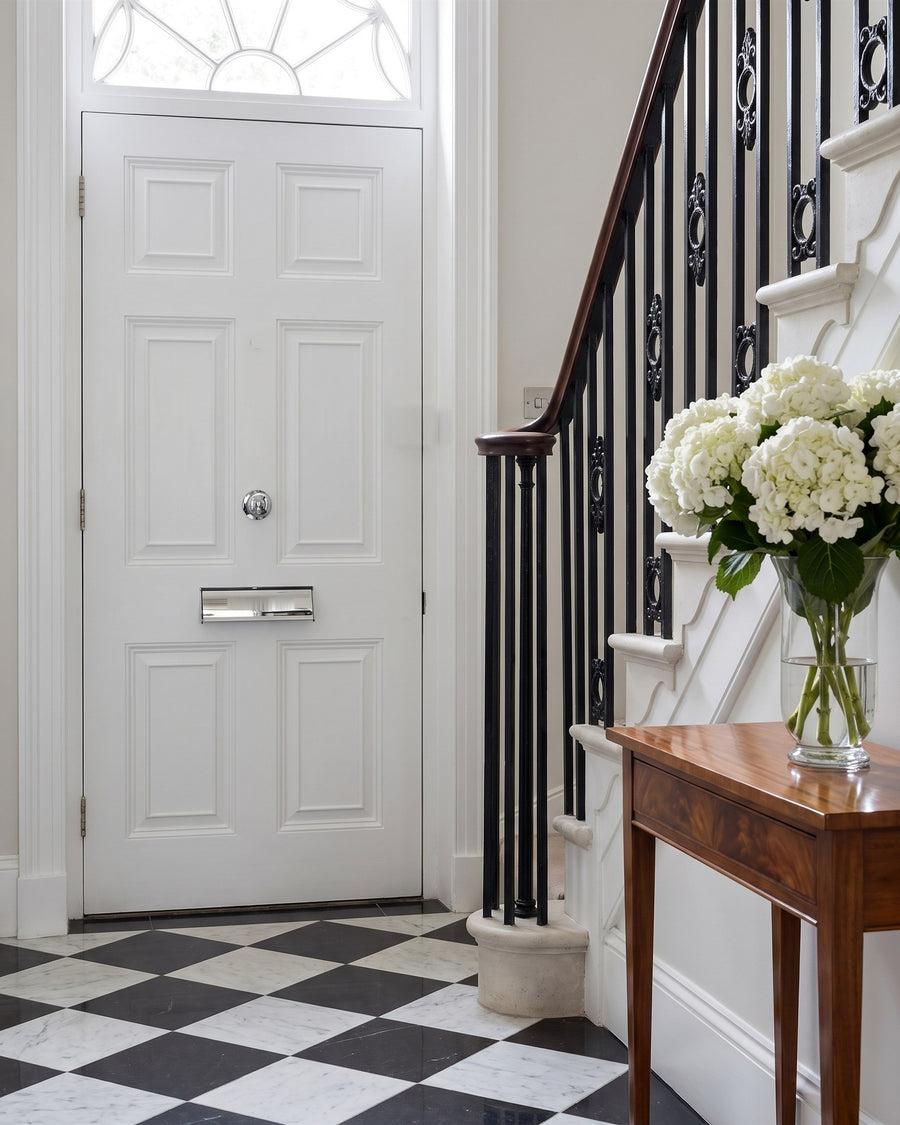 Regency entrance hall with a black and white marble floor, iron balustrade, hydrangeas and a chrome letter tidy on the white inside of the front door