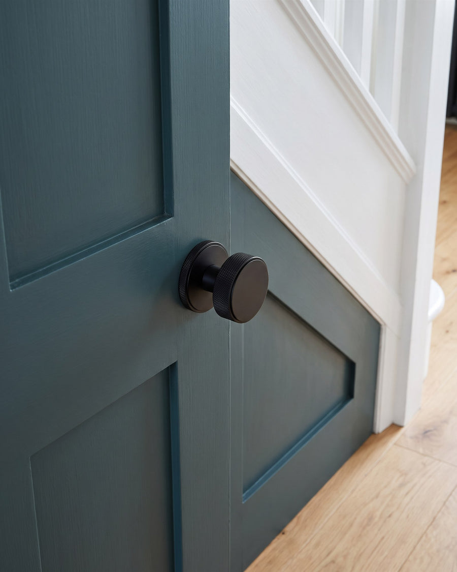 Matt black knurled mortice knob on a deep green understairs cupboard door