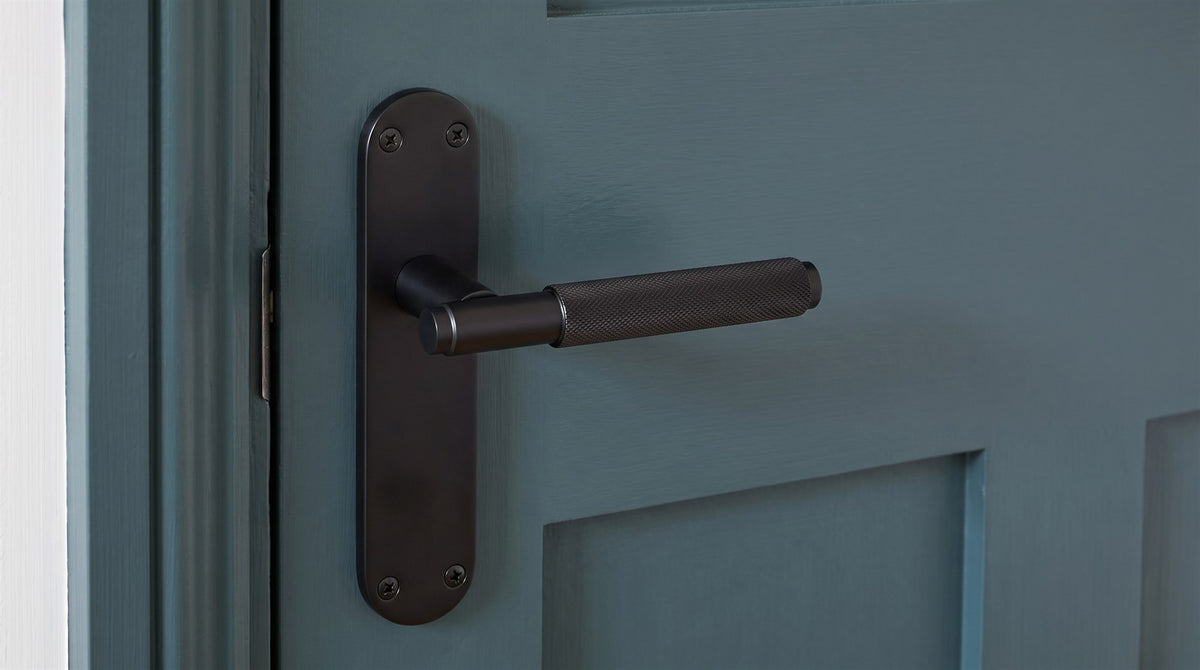 Matt black Connaught lever with a finely knurled round grip on a slim backplate with rounded ends, on a deep smoky green panelled door