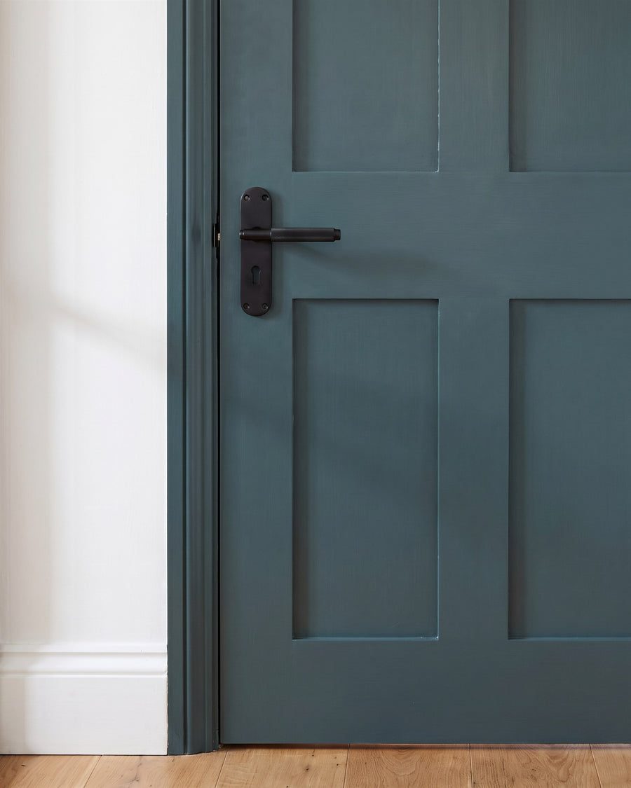Matt black Connaught knurled lock handle with a keyhole on a deep green four-panel door