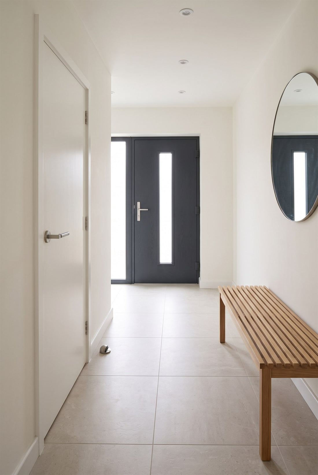 Contemporary entrance hall with porcelain floor, a warm white flush door with a satin nickel Bauhaus lever on rose and a hooded floor stop, and an anthracite composite front door with a matching multipoint handle