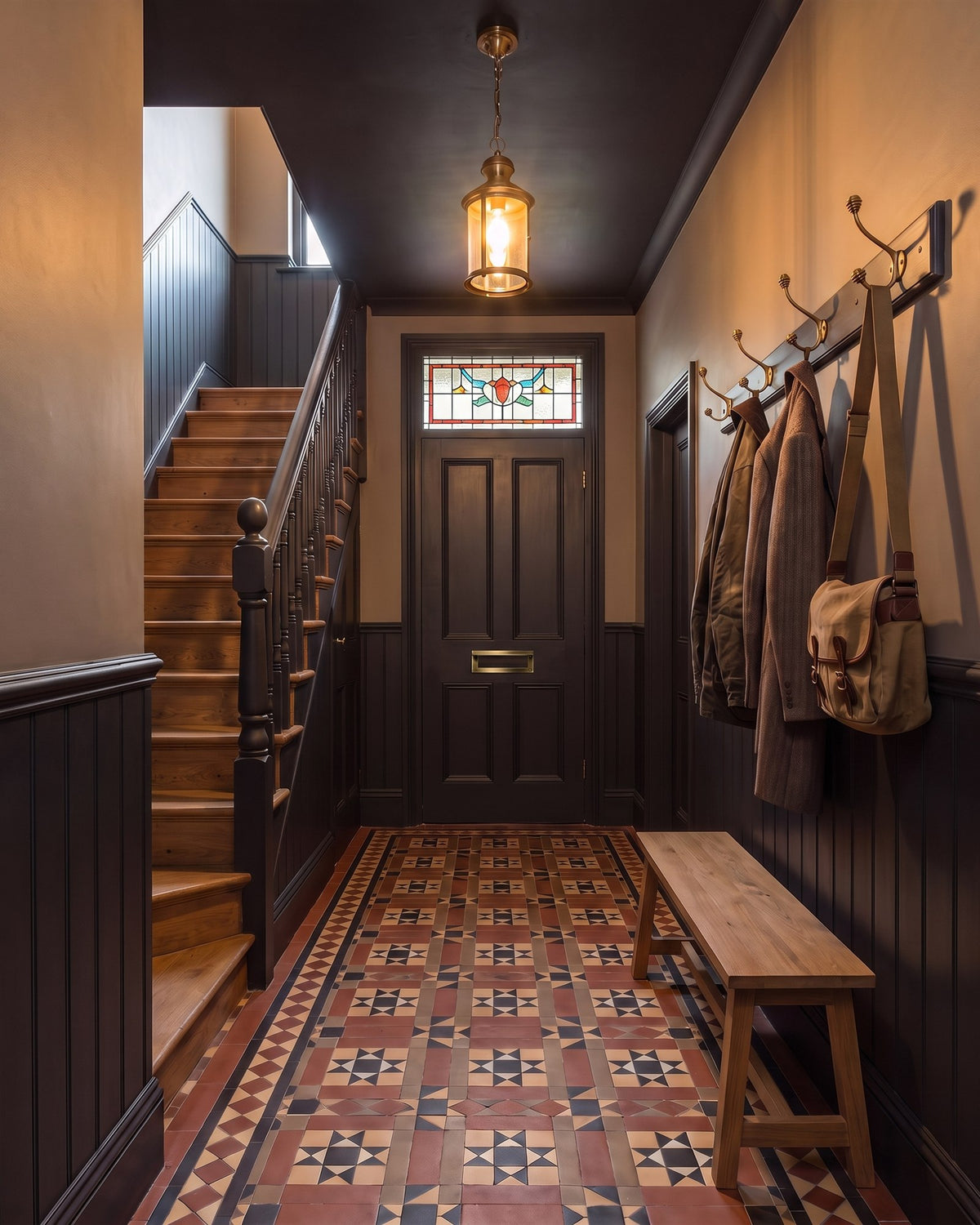 Victorian hall with off-black panelling and ceiling, a stained glass fanlight over the front door, encaustic tiles, a staircase and aged brass coat hooks over an oak bench