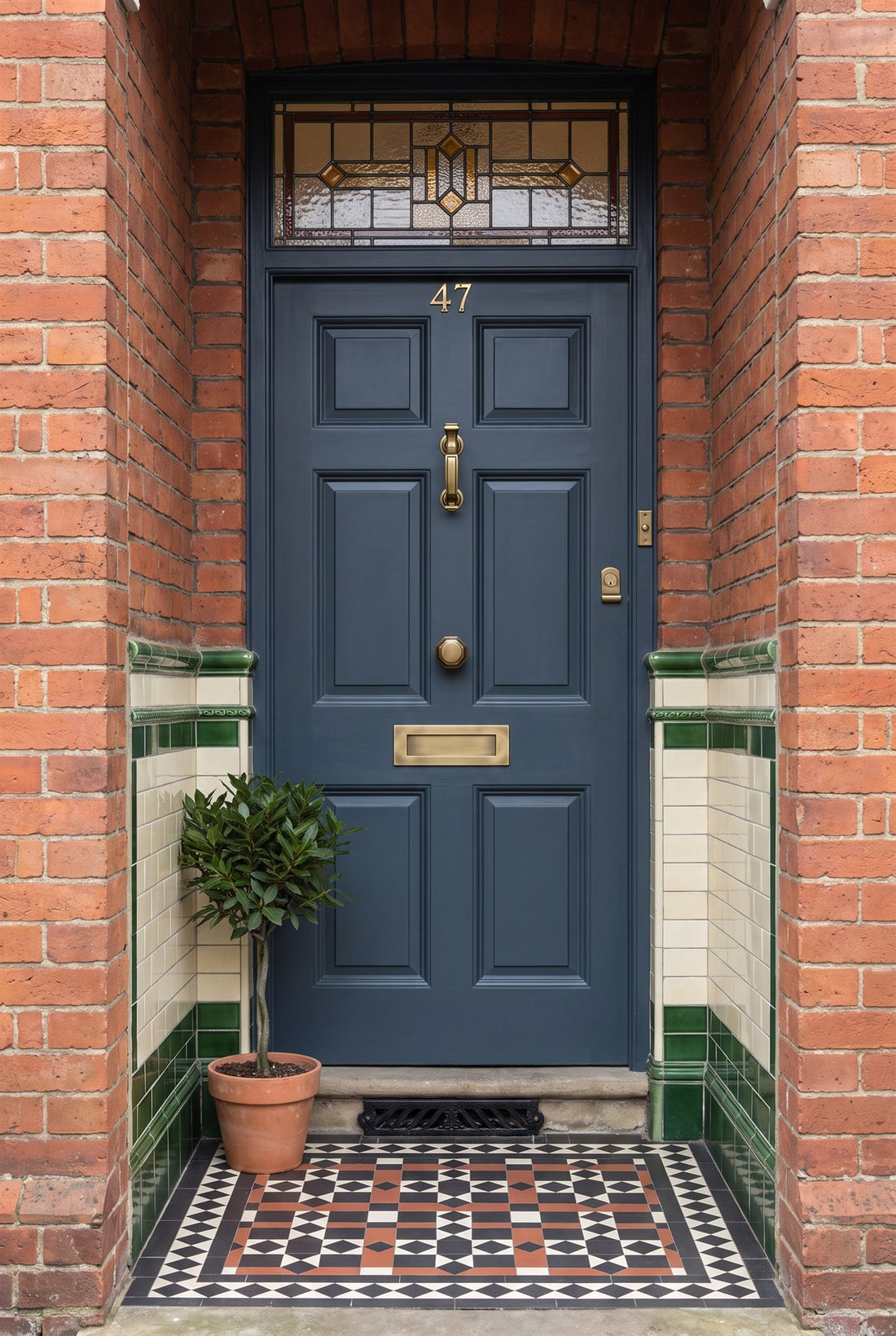 Dark blue-grey four-panel Victorian front door with a leaded stained-glass fanlight in a tiled porch, fitted with antique brass numbers 47, doctor knocker, octagonal centre knob, letter plate, cylinder pull and bell push