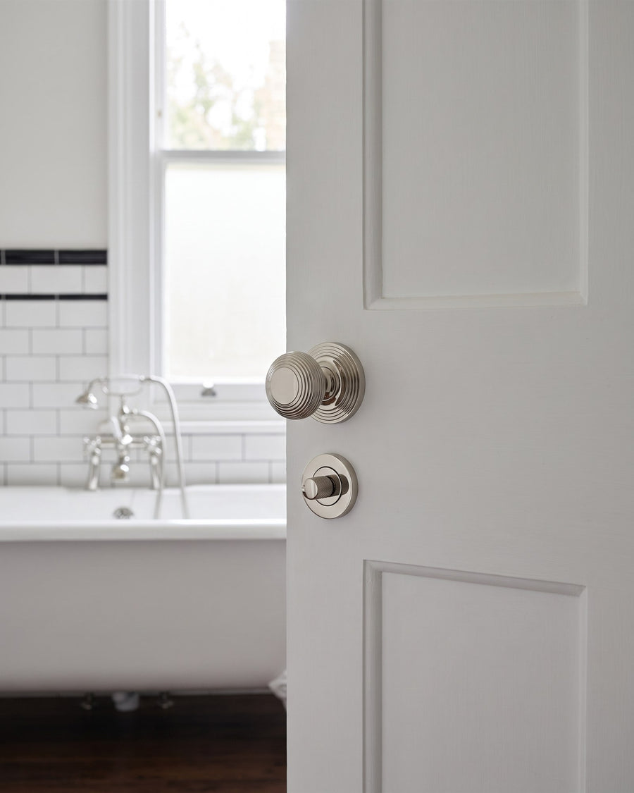 Edwardian bathroom door with a polished nickel reeded knob and matching thumbturn below, roll-top bath beyond