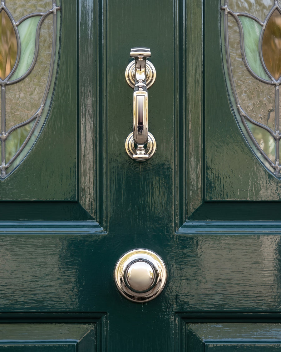 Polished nickel doctor knocker above a polished nickel centre door knob on a deep green door between leaded glass panels