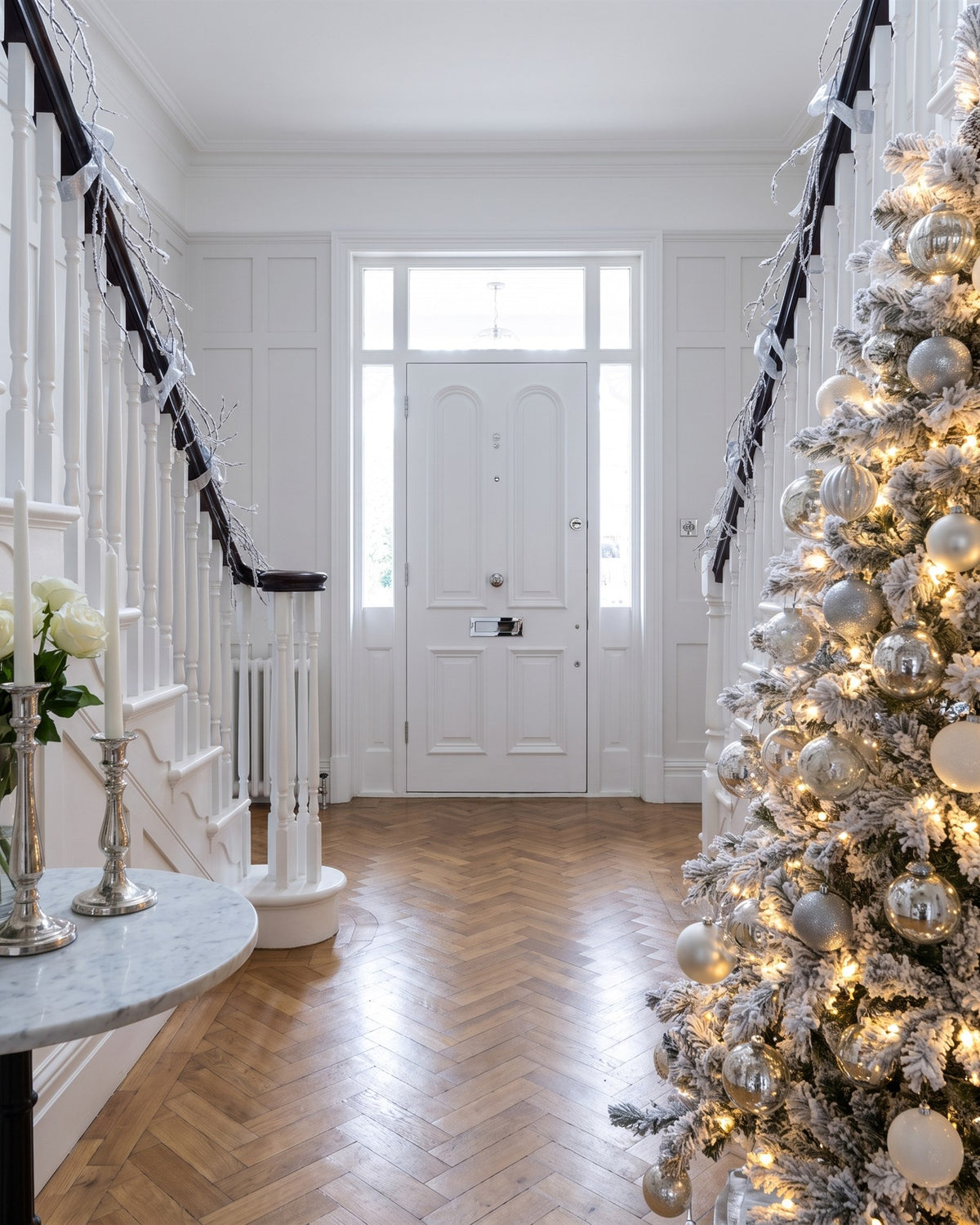 Edwardian hallway with herringbone parquet, white panelling and a white flocked Christmas tree in silver and white, looking towards the inside of the front door